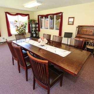 A well-furnished dining room with a large wooden table and chairs, adorned with decorative elements and natural light from large windows.