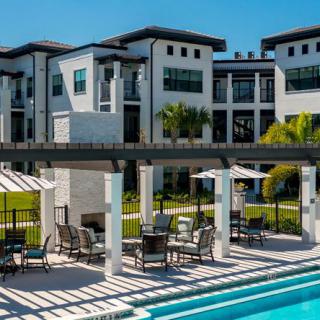 A modern apartment complex featuring an outdoor pool with surrounding patio furniture.
