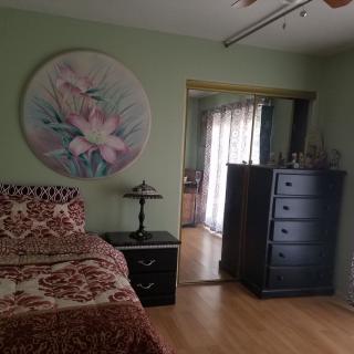 A cozy bedroom with a floral artwork on the wall, featuring a bed, nightstand, and dresser.