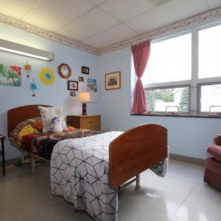 A cozy nursing home room with a single hospital bed, decorated walls, and a window with red curtains.