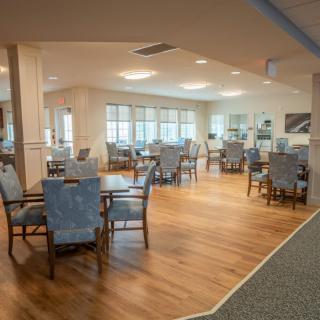 A spacious and well-lit dining area with several tables and chairs arranged neatly on a wooden floor.