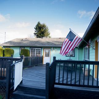 A residential house with an American flag on display and a wooden patio under a clear blue sky.