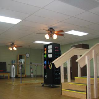A spacious room featuring ceiling fans, a set of stairs, and various furniture arrangements.