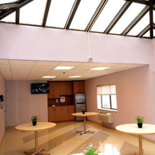 A modern office lounge area featuring tables, plants, and a television.