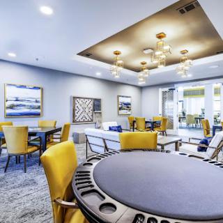 A modern lounge area featuring a poker table surrounded by vibrant yellow chairs, perfect for socializing and game nights.