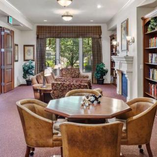 A cozy living room with a table and chairs, surrounded by bookshelves and large windows.