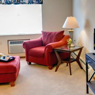 A cozy living room with a red armchair and ottoman, accompanied by a side table and lamp beside a television.