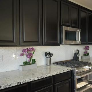 A modern kitchen with dark cabinets, light speckled countertops, and stainless steel appliances.