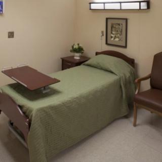 A tidy hospital room with a single bed, chair, and over-bed table.