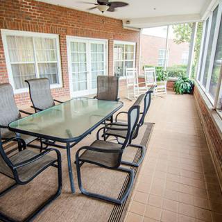 A spacious screened patio with a glass dining table and chairs, set against a brick wall, featuring large windows and a ceiling fan.