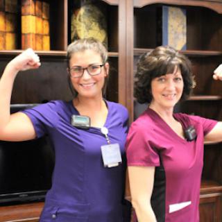 Two nurses proudly flexing their arms and smiling.