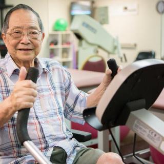 An elderly man exercising on fitness equipment in a gym setting.