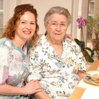 Two women, possibly family members, sitting together and smiling indoors.
