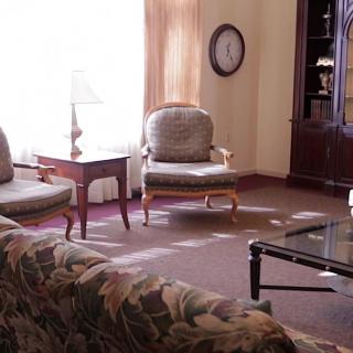 A cozy living room with chairs, a sofa, a table, and a lamp.