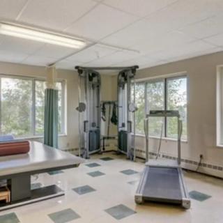 A small, well-lit exercise room featuring a treadmill and other gym equipment with large windows.