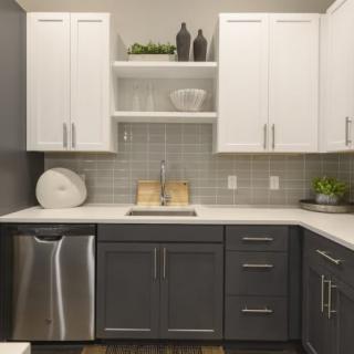 A modern kitchen with white upper cabinets, dark lower cabinets, and stainless steel appliances.