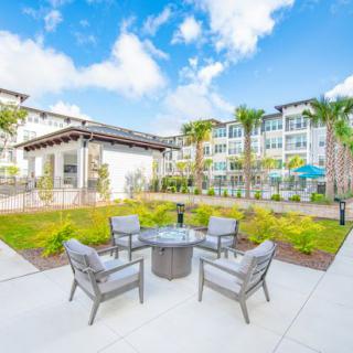 A sunny day view of a modern apartment complex with an inviting outdoor patio area and lush garden.