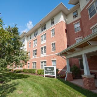 A brick residential apartment building with a green lawn and clear blue sky.