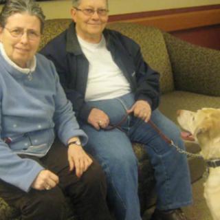 An elderly couple sitting on a sofa with a dog nearby.