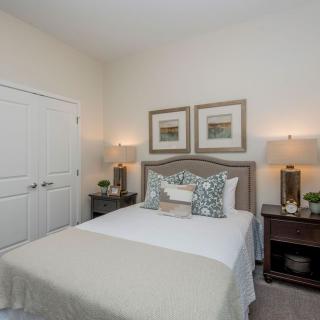 A cozy bedroom with a neatly made bed, matching nightstands and lamps, and framed artwork above the headboard.