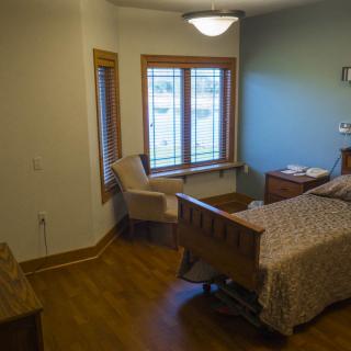 A cozy bedroom with a single bed, chair by the window, and hardwood flooring.