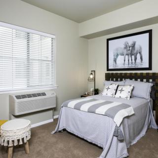 A modern bedroom featuring a neatly made bed, a large piece of artwork above the headboard, and a window with blinds.