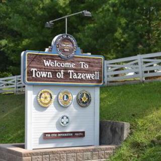 A welcome sign for the Town of Tazewell featuring various emblems and greenery in the background.