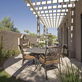 A sunny patio with a pergola and outdoor furniture, featuring a table and chairs surrounded by a well-maintained garden.