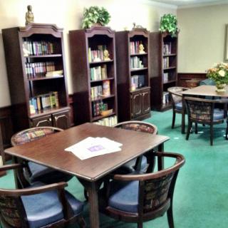 A cozy library reading room with tables, chairs, and bookshelves.
