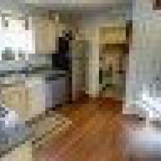 A modern kitchen featuring wooden floors, cream-colored cabinets, and stainless steel appliances.