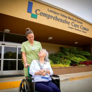 A healthcare worker assists an elderly patient in front of the Comprehensive Care Center.