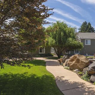 A well-landscaped garden with a pathway leading to a house, surrounded by lush greenery and rocks.