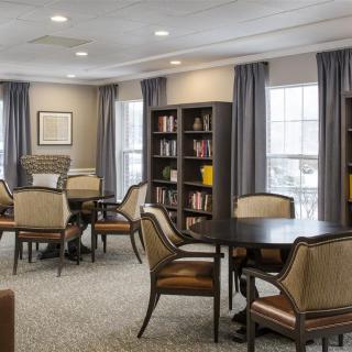 A cozy library room with bookshelves, tables, and chairs arranged for reading and relaxation.