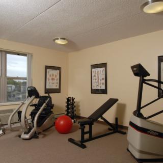 A small gym with various exercise equipment, including an elliptical machine, bench, dumbbells, and a red exercise ball.