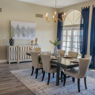 A modern dining room featuring an elegant chandelier, stylish table settings, and navy blue curtains.