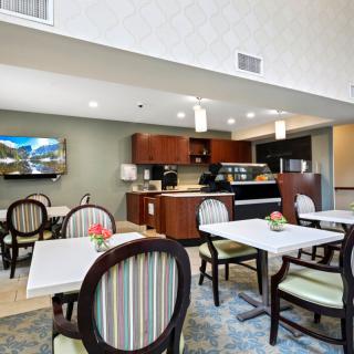 A modern dining area with tables and chairs, featuring a small kitchenette in the background.