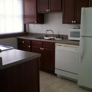 A kitchen with dark wood cabinets, a refrigerator, a microwave, and a dishwasher.
