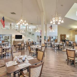 A spacious, elegantly decorated dining area with neatly arranged tables and chairs, featuring chandeliers and a wooden floor.
