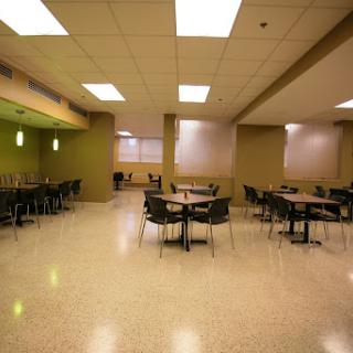 An empty modern dining area featuring round tables and chairs, illuminated by overhead lighting.
