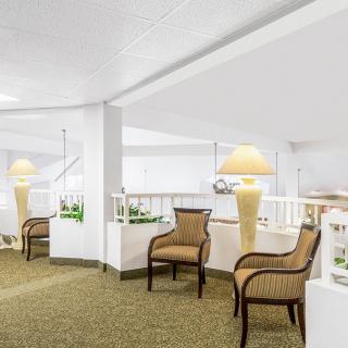 A modern lobby seating area with wicker chairs, large lamps, and a carpeted floor.