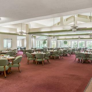 A spacious dining area with multiple tables and chairs, featuring large windows and ceiling fans.