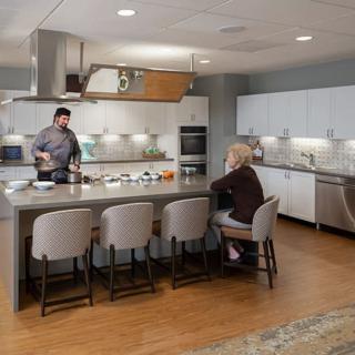 A modern kitchen with a person cooking and another sitting at the island counter.