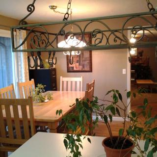A cozy dining room with a wooden table, chairs, hanging lights, and indoor plants.