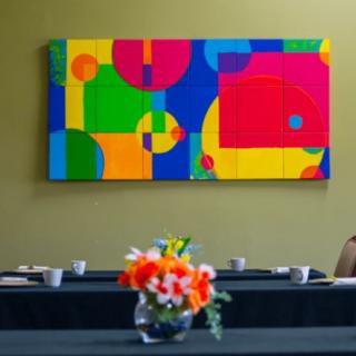 A colorful abstract painting hangs on the wall of a conference room, with a bouquet of flowers in a vase on the table.