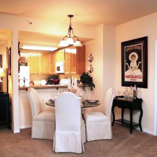 A cozy dining area with a small round table adjacent to a warm-lit kitchen, featuring elegant decor and wall art.