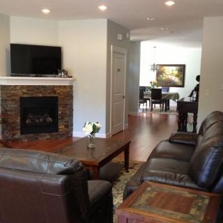 A modern living room featuring a stone fireplace and wall-mounted TV, with comfortable sofas and a view into the dining area.