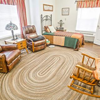 A cozy bedroom with a single bed, leather chairs, a rocking chair, and a braided rug.