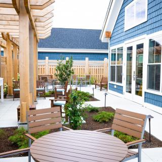 A cozy outdoor patio with wooden furniture and a pergola, adjacent to a modern blue house.