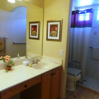 A well-lit bathroom with a large mirror, decorated with artwork and a flower arrangement on the counter.