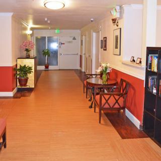A well-decorated hallway with wooden flooring, featuring chairs, tables, and potted plants.
